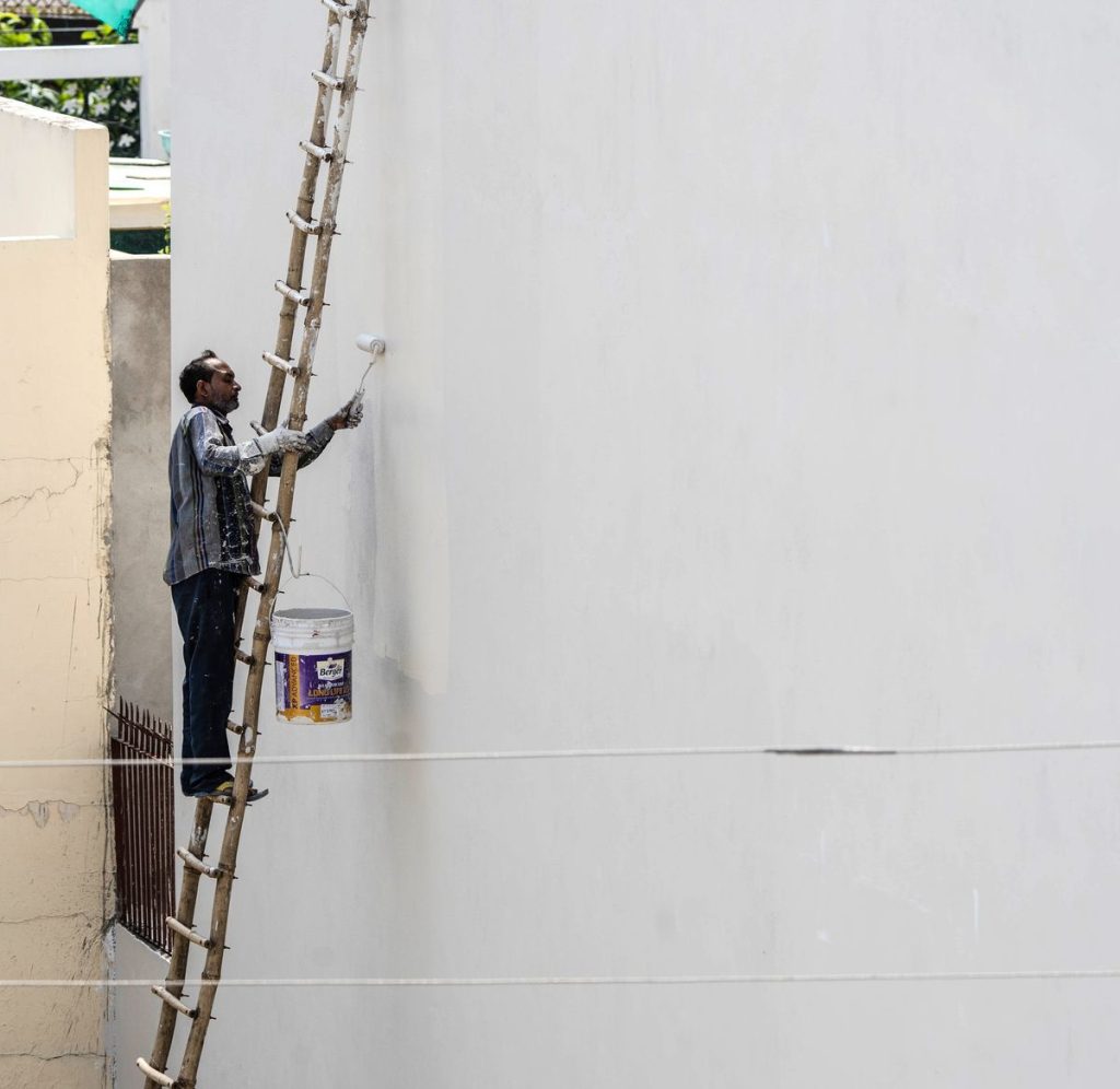 Painter on a ladder painting a house exterior wall