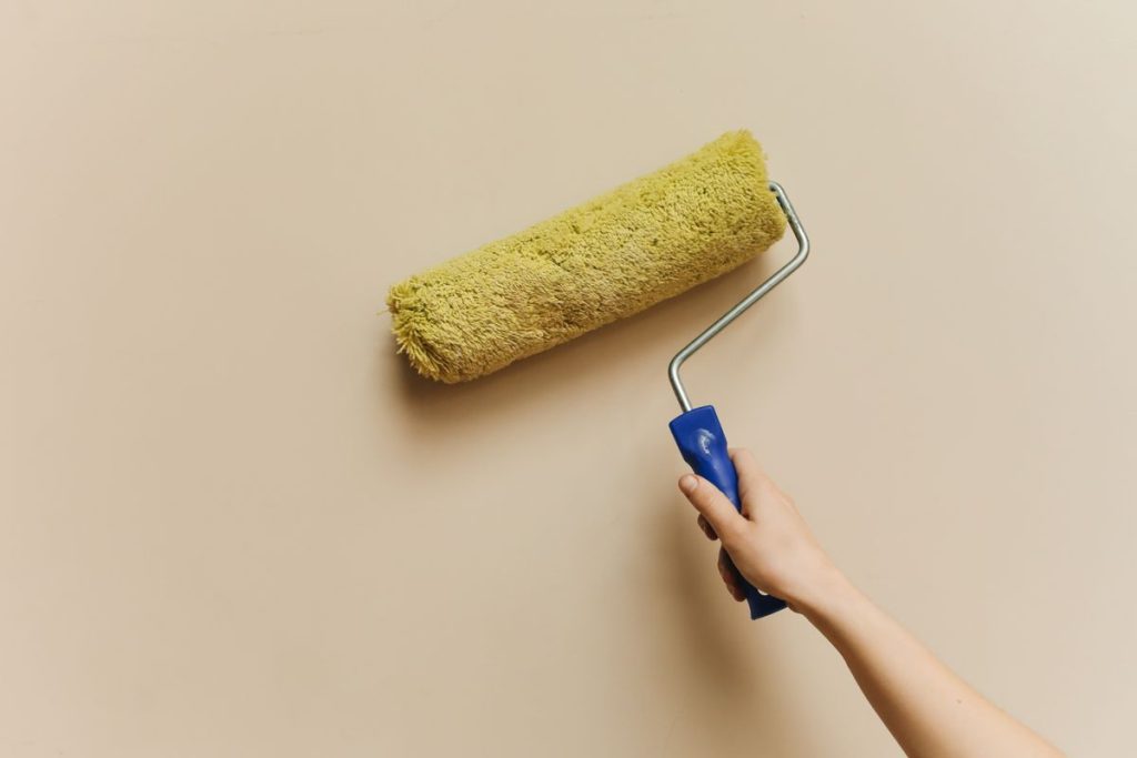 Hand repainting a wall with a yellow paint roller