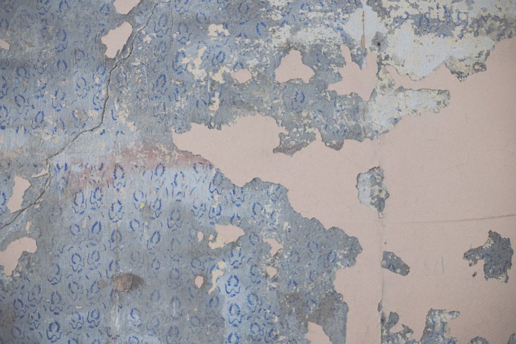 Old wallpaper peeling away from a damp plaster wall