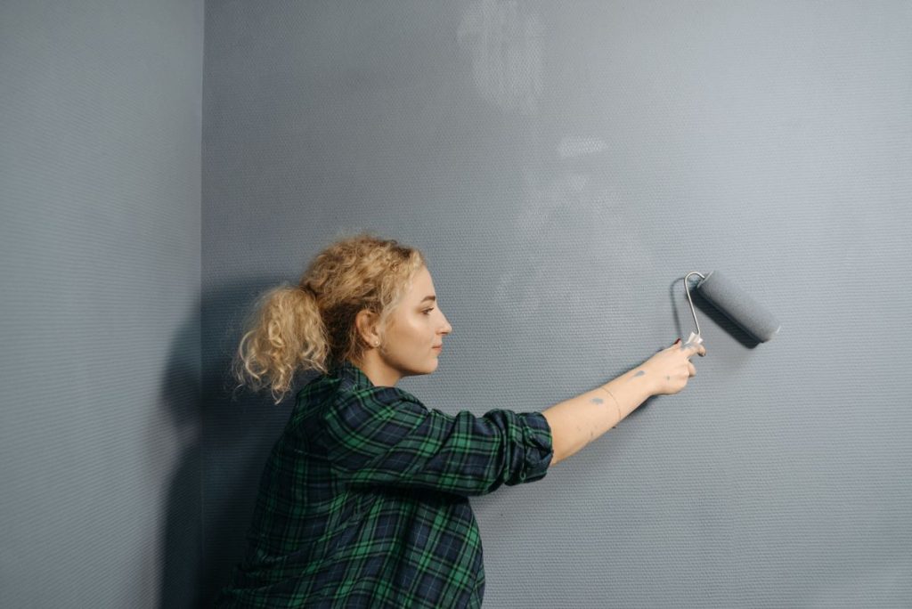 Applying a second coat of grey emulsion to an interior wall with a roller